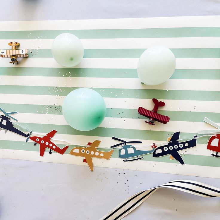 an assortment of toy airplanes and balloons on a striped tablecloth with silverware next to it