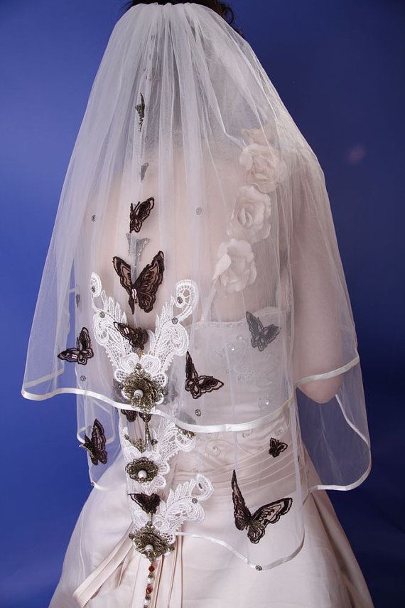 a white wedding dress with butterflies on the back and veil over her head, in front of a blue background