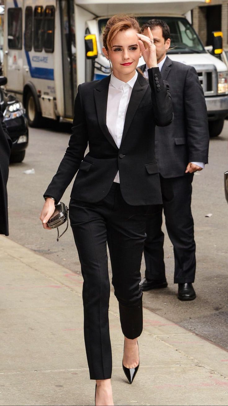 a woman in a suit walking down the street with her hand up to her face