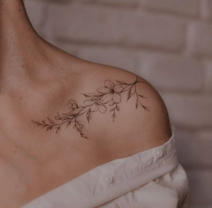 a woman with a tattoo on her shoulder is wearing a white dress and has flowers in the back