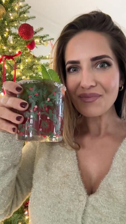 a woman is holding a glass with flowers in it while standing next to a christmas tree