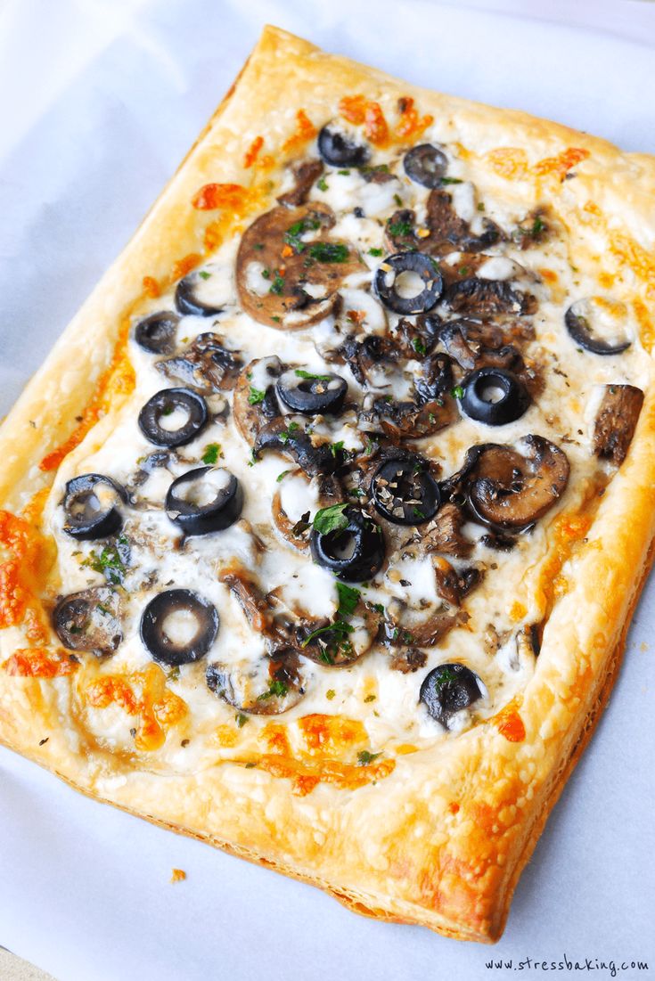 a square pizza with mushrooms and cheese is on a piece of wax paper, ready to be eaten