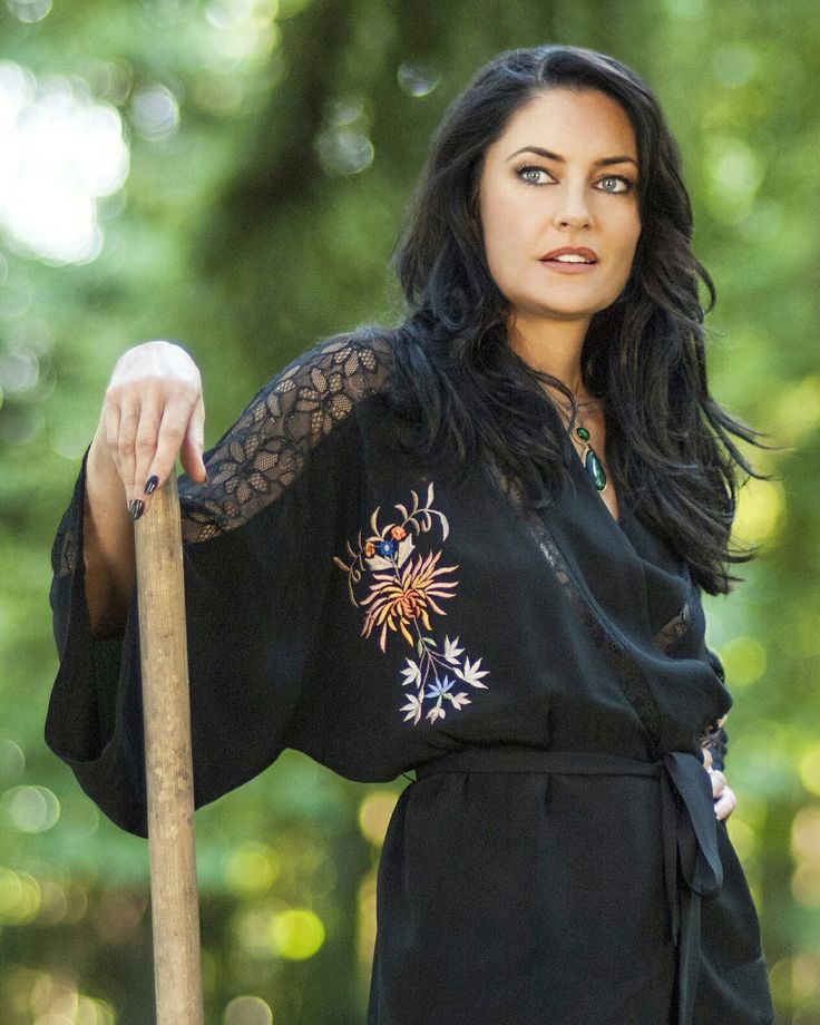 a woman holding a wooden stick in her right hand and wearing a black dress with floral embroidery on it