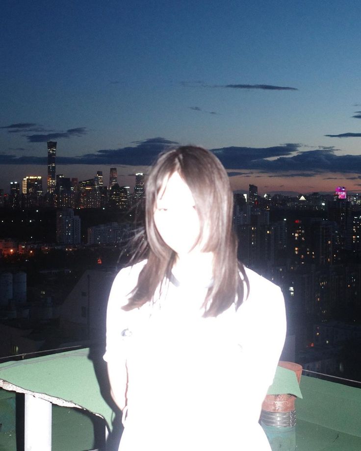 a woman standing on top of a roof next to a tall building at night with the city lights in the background