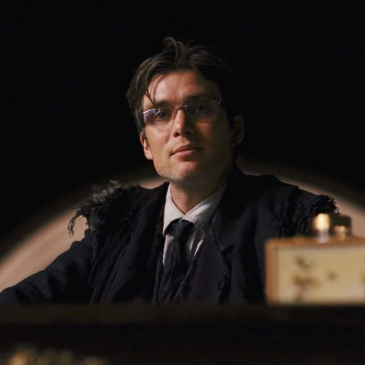 a man with glasses sitting at a table in front of a clock and candlelight