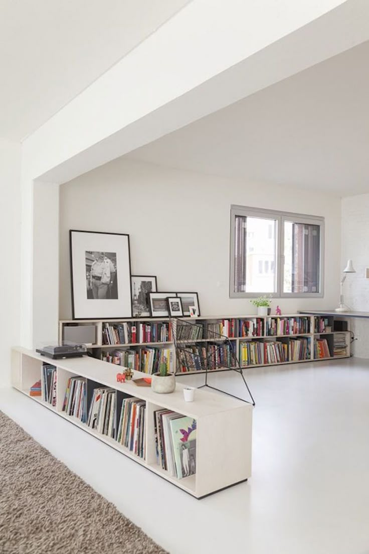 a living room filled with lots of books on top of a white book shelf next to a window