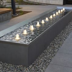 an outdoor water feature with lights on the sides and pebbles in the ground next to it