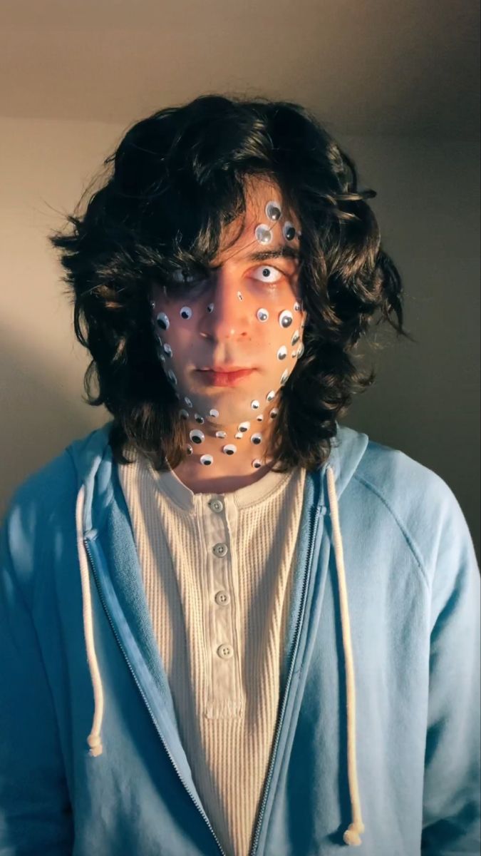 a man with his face painted white and wearing a blue hoodie is standing in front of a wall