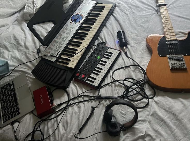 an electronic keyboard, headphones and guitar are on a bed