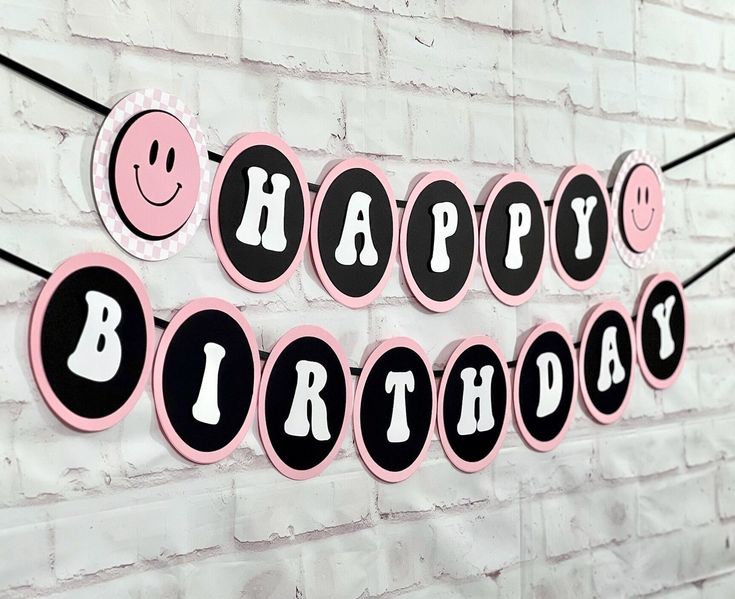 a happy birthday banner on a brick wall with pink and black decorations hanging from it