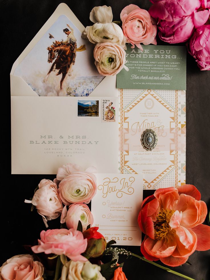 the wedding stationery is surrounded by pink flowers and greenery, including peonies