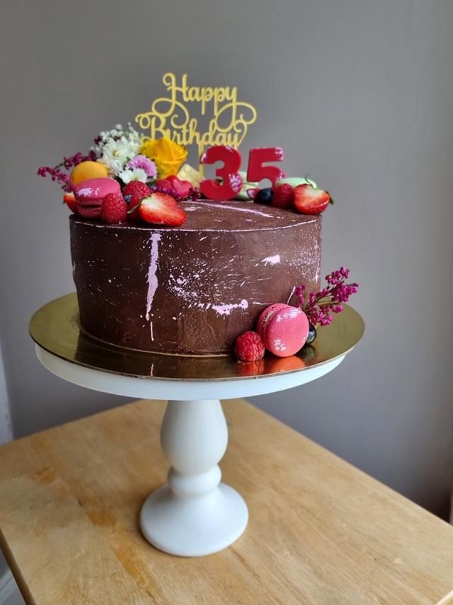 a chocolate birthday cake with strawberries and flowers on a wooden table in front of a gray wall