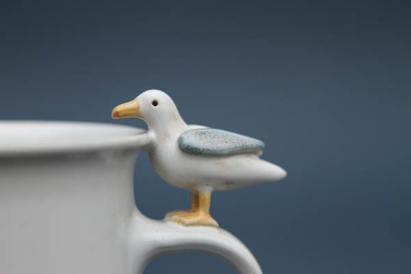 a ceramic bird figurine sitting on top of a coffee cup in front of a gray background