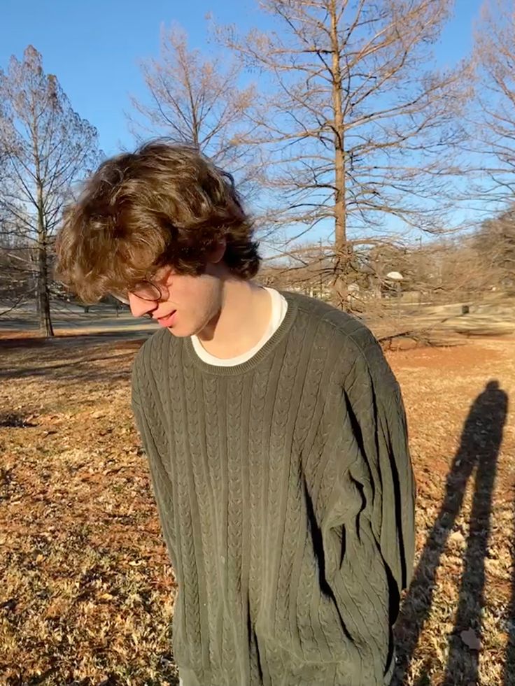 a young man standing in the grass with his shadow cast on him's sweater