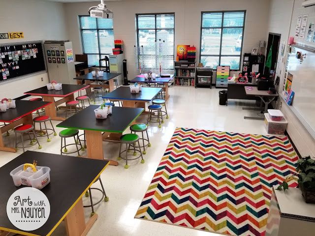 an empty classroom with desks, chairs and colorful rug on the floor in front of windows