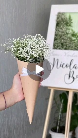 a person holding a paper cone with baby's breath in front of a sign