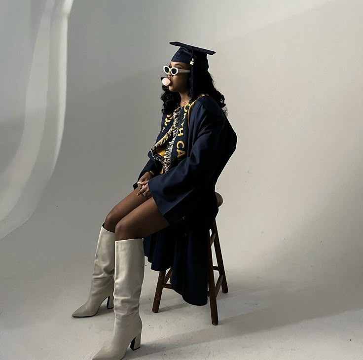 a woman sitting on top of a wooden chair wearing boots and a graduation cap with her legs crossed