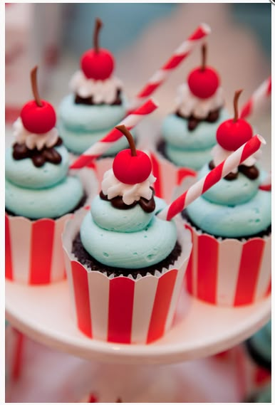 cupcakes with blue frosting and cherries are on a cake plate, ready to be eaten