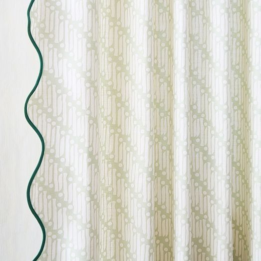 a curtain with green trim hanging on the side of a white wall next to a window