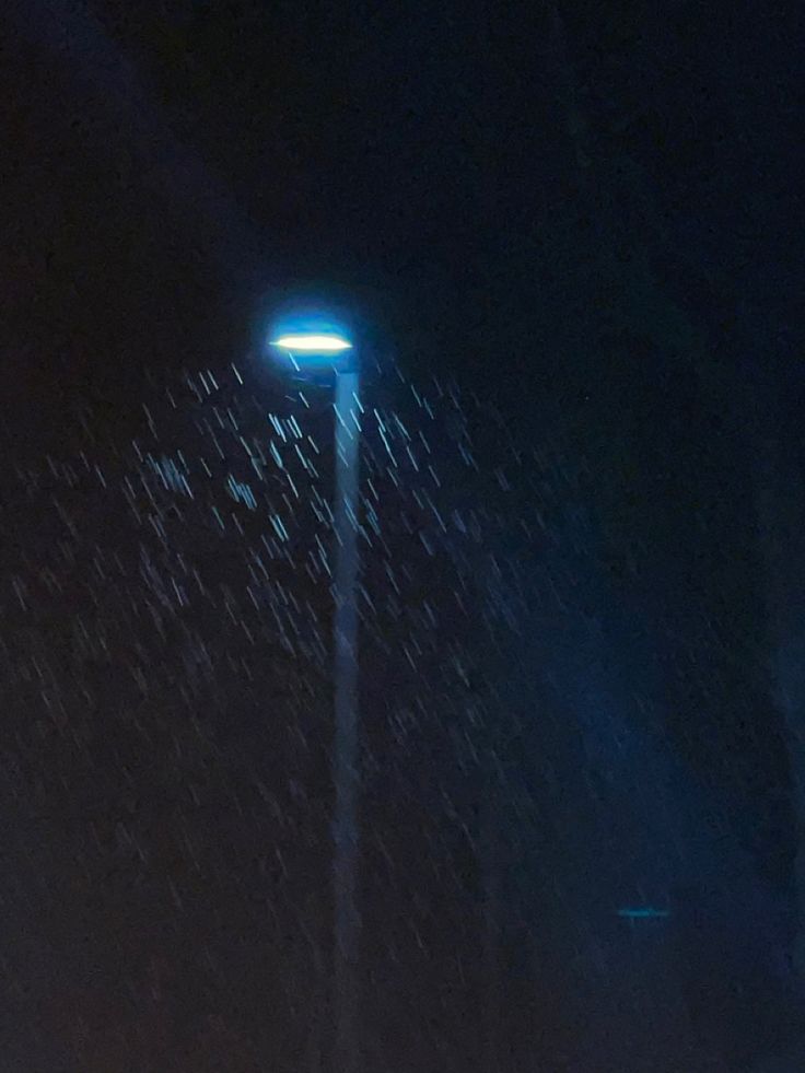 a street light in the dark with rain coming off it's sides and on its side