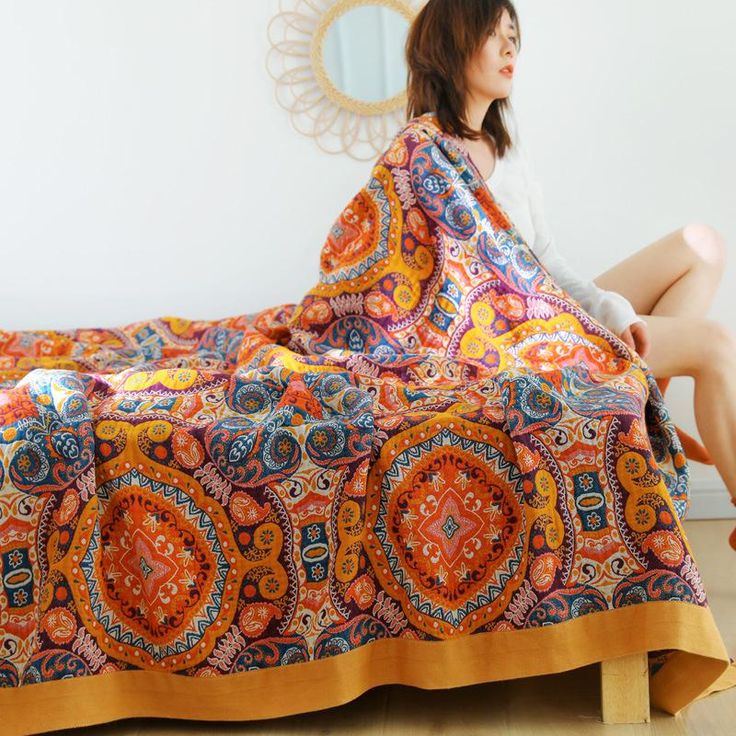 a woman sitting on top of a bed covered in a colorful blanket