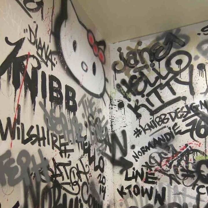 graffiti is on the wall next to a toilet in a public restroom with walls covered in black and white writing