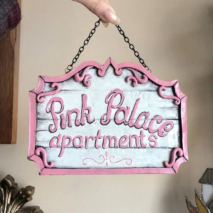 a pink and white sign that says pink palace apartments hanging from a hook on a wall