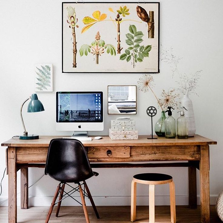 a wooden desk topped with a computer monitor next to a black chair and a painting on the wall