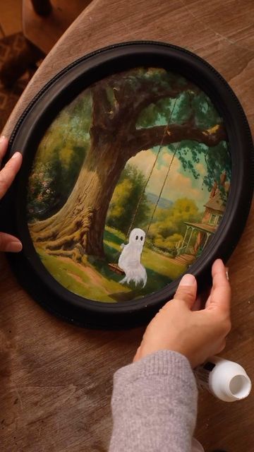 a person holding a painting with a ghost on it in front of a wooden table