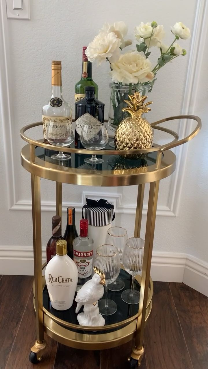 a gold bar cart filled with liquor bottles and wine glasses on top of a hard wood floor