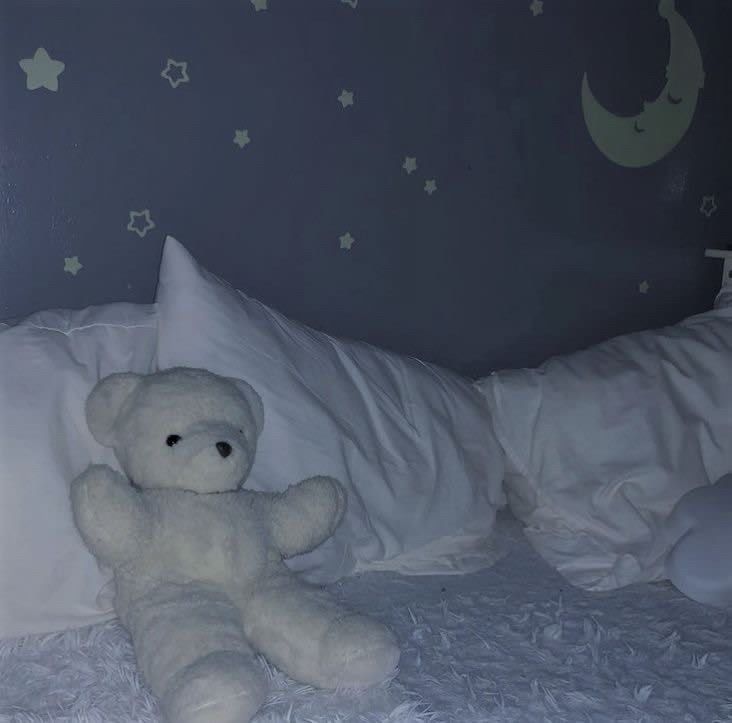 a white teddy bear sitting on top of a bed next to pillows and pillow cases