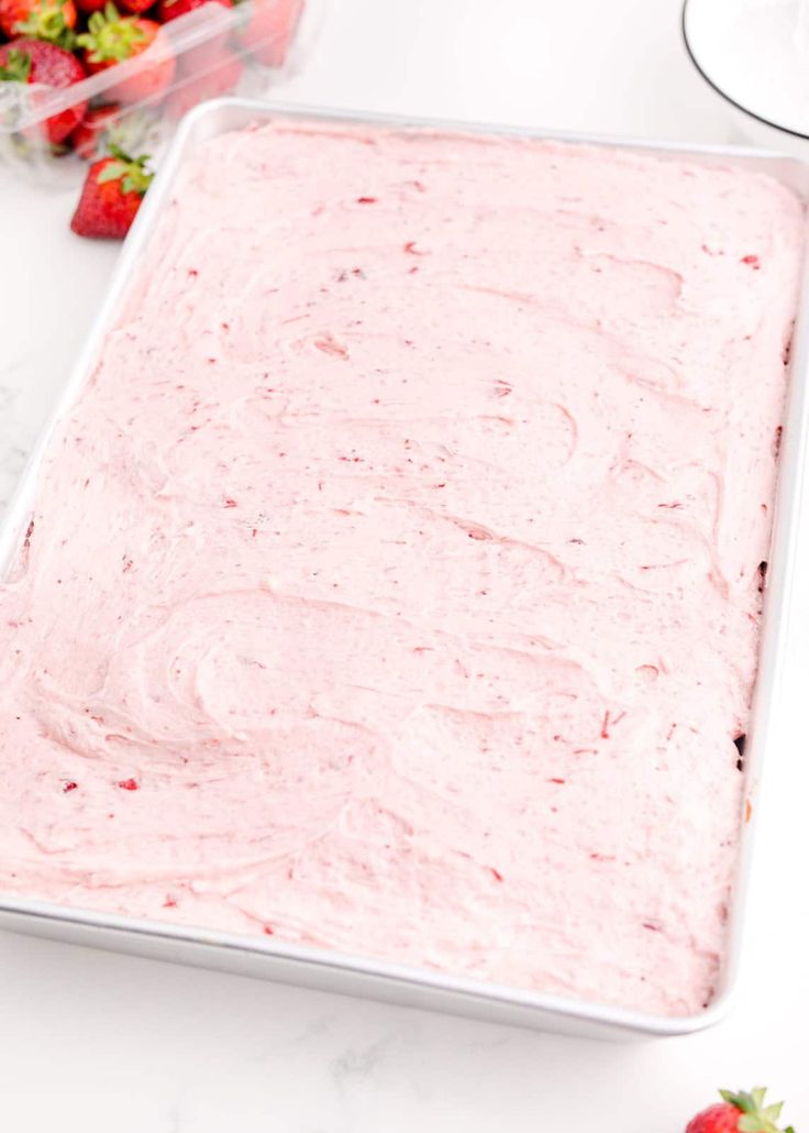 a pan filled with strawberry cake batter next to some strawberries on the counter top