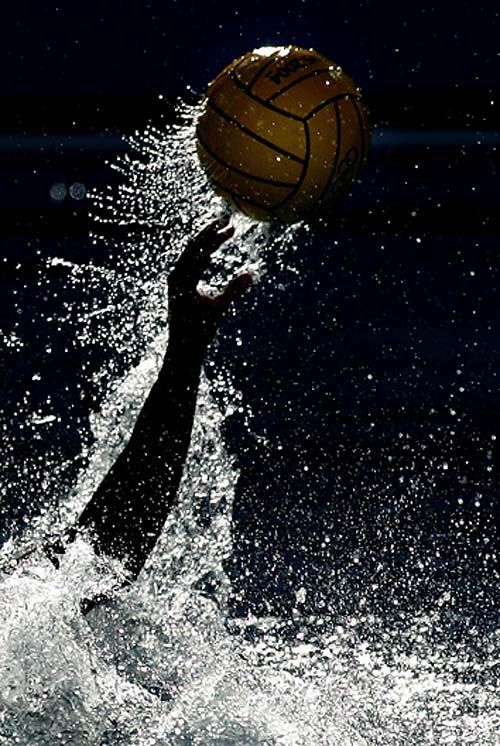 a person jumping up into the air to hit a ball with their hands in the water