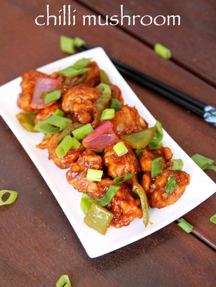 chicken with peppers and onions on a white plate next to chopsticks in the background