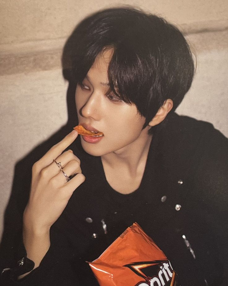 a young man eating an orange candy bar while wearing a black jacket and holding a ring on his finger