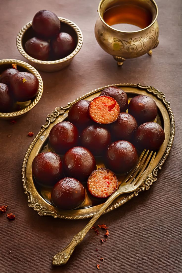 plums in gold dishes with orange juice and spoon on brown tablecloth next to two bowls