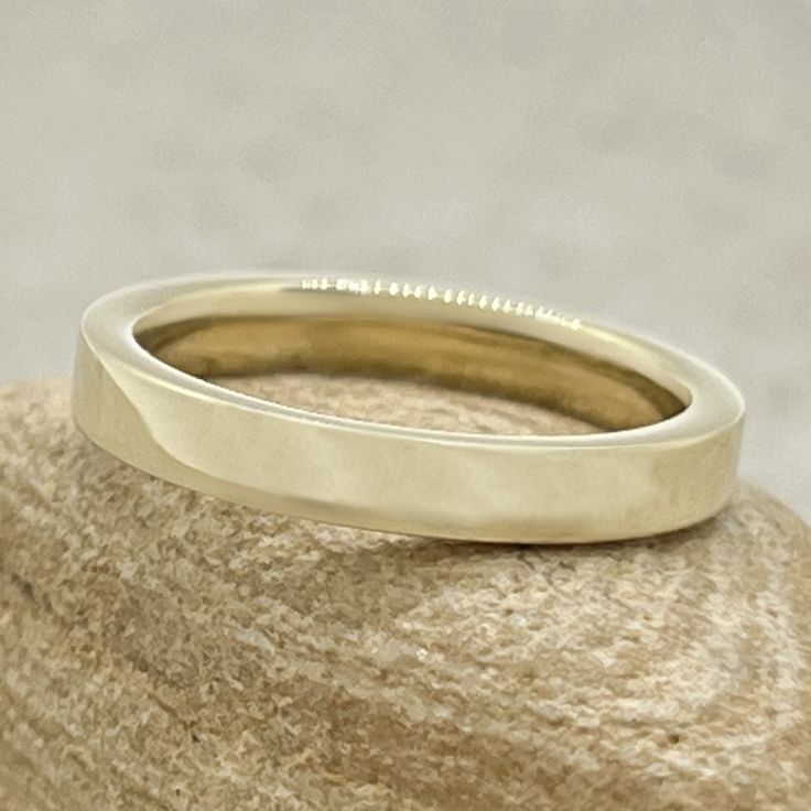 a yellow gold wedding ring sitting on top of a rock