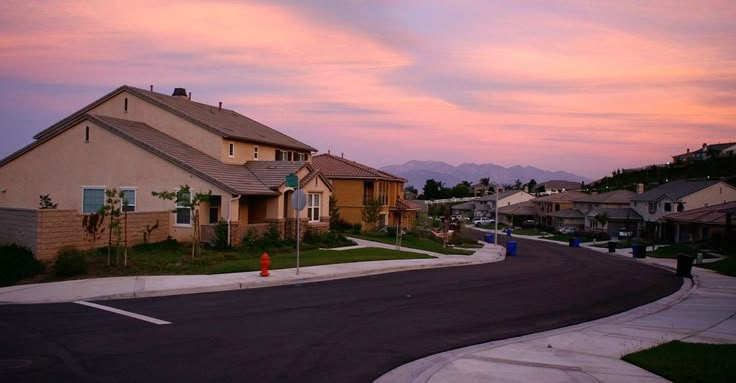 a street with houses on both sides and mountains in the background at sunset or dawn