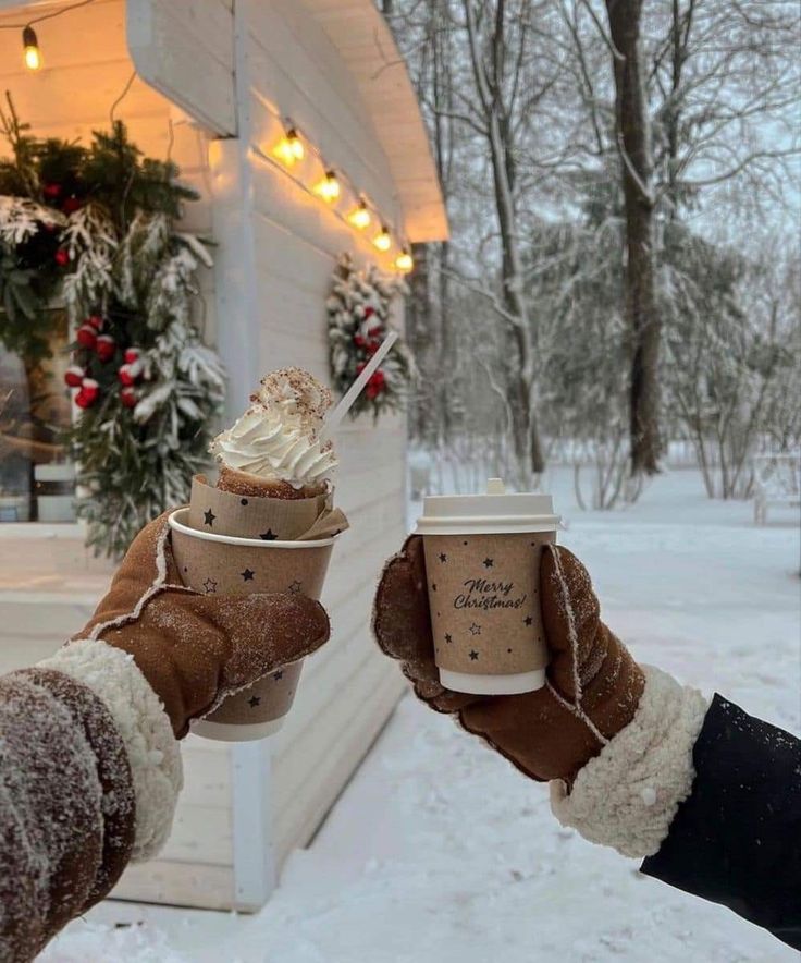 two people holding up coffee cups in the snow