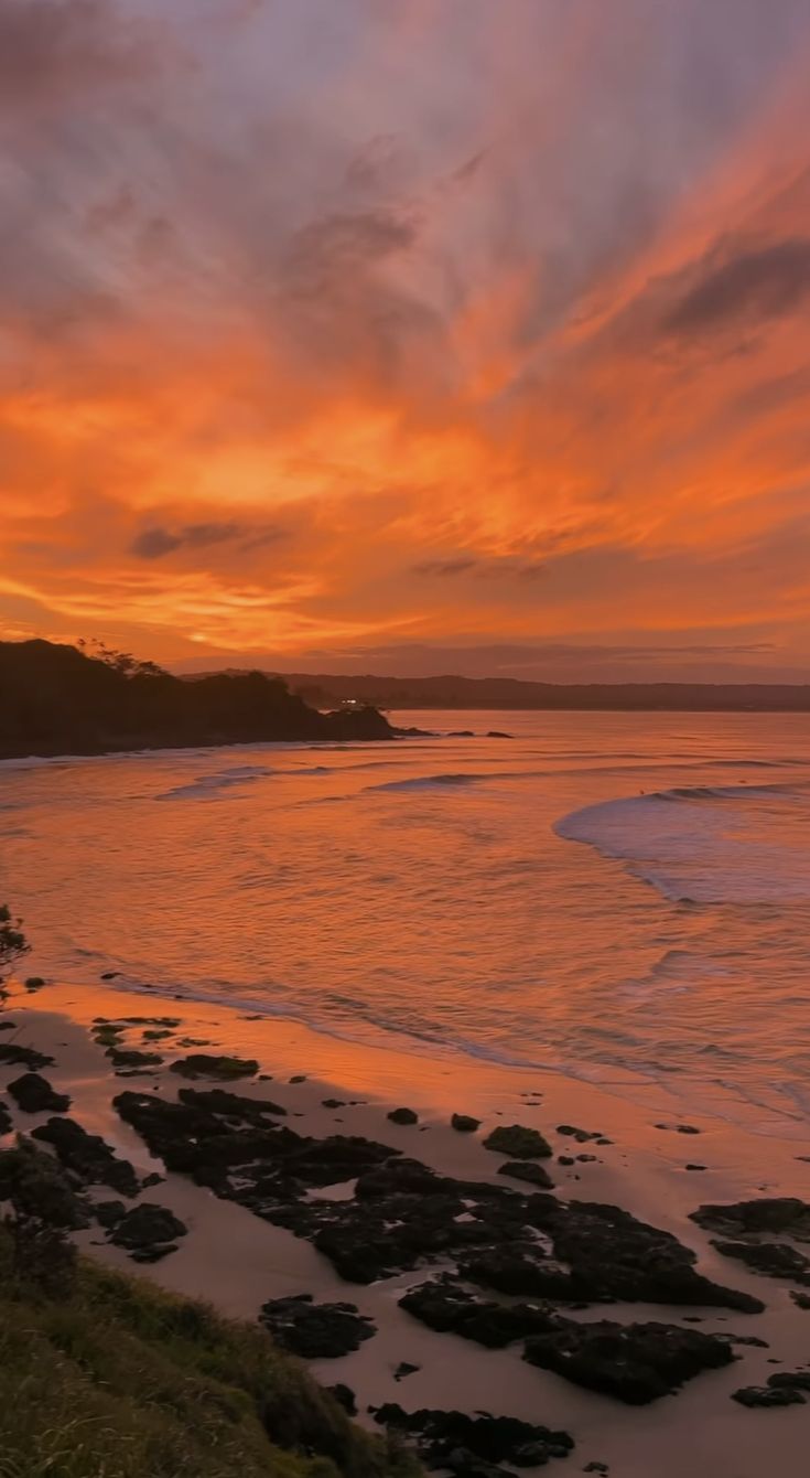 the sun is setting over an ocean with rocks