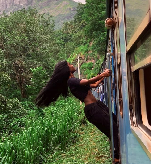 a woman leaning out the window of a train as it travels through lush green countryside