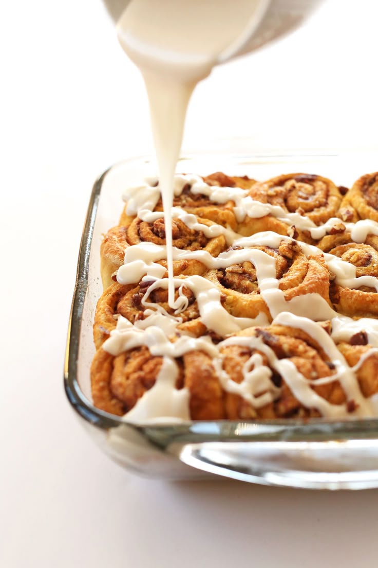 a person pouring milk on top of a cinnamon roll in a glass baking dish with white icing