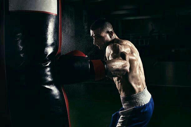 a shirtless man wearing boxing gloves is in the dark with his hand on a punching bag