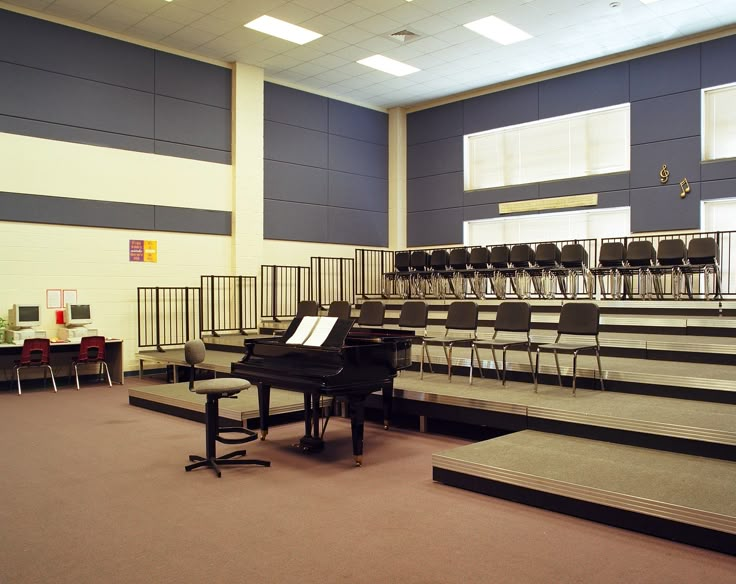 an empty auditorium with chairs and piano on the floor in front of it, as well as steps leading up to them