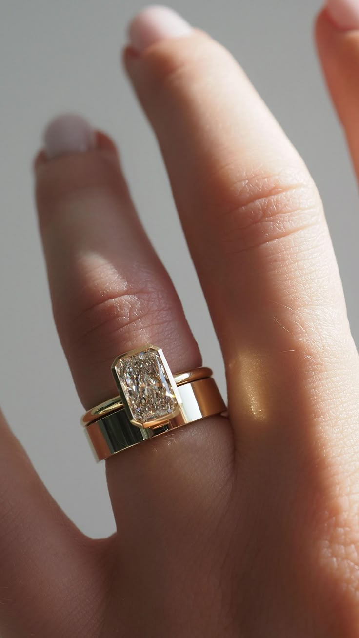 a woman's hand with two gold rings on top of her finger and the ring has a diamond in it