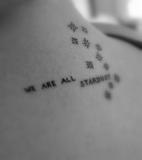 we are all stardust tattoo on the back of a woman's left shoulder