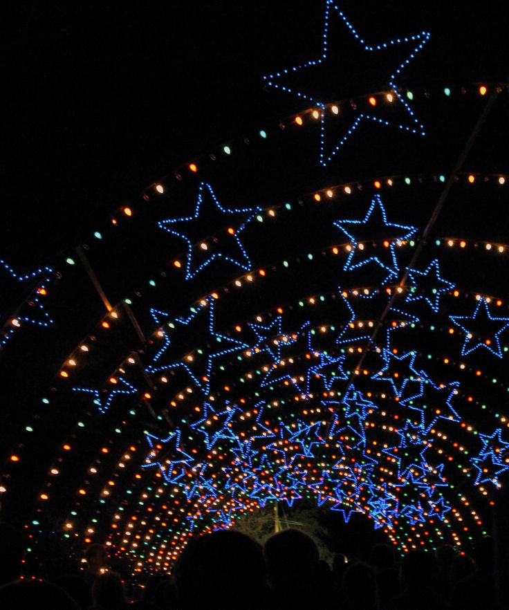 people are standing under an archway decorated with lights and stars in the dark, all lit up at night