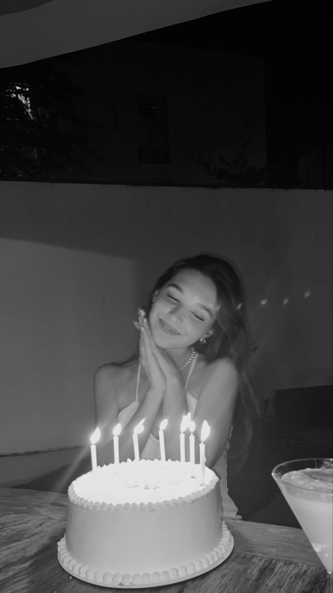 a woman sitting in front of a white cake with lit candles on top of it