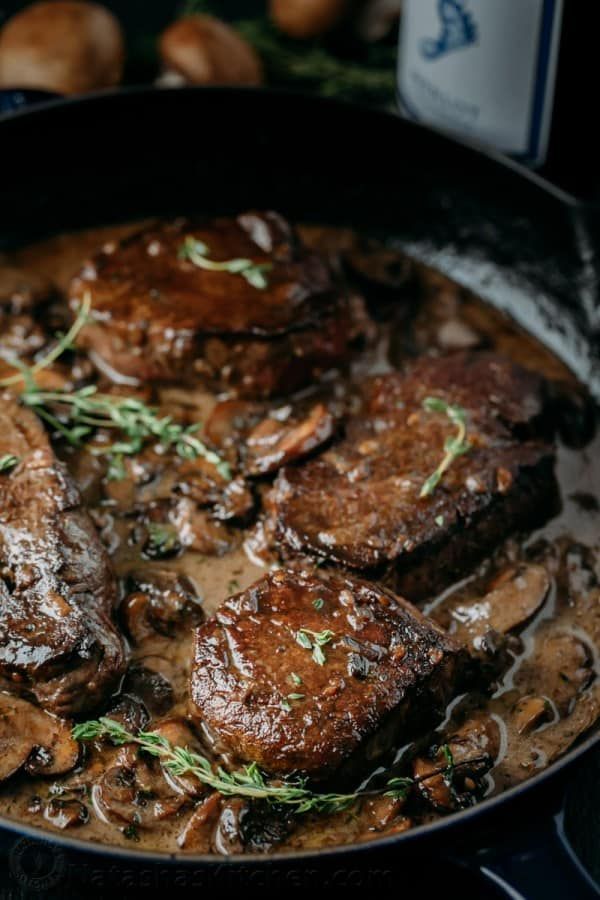 steaks and mushrooms are cooking in a skillet with gravy on the side