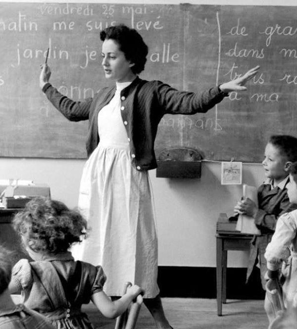 a woman teaching children in front of a chalkboard